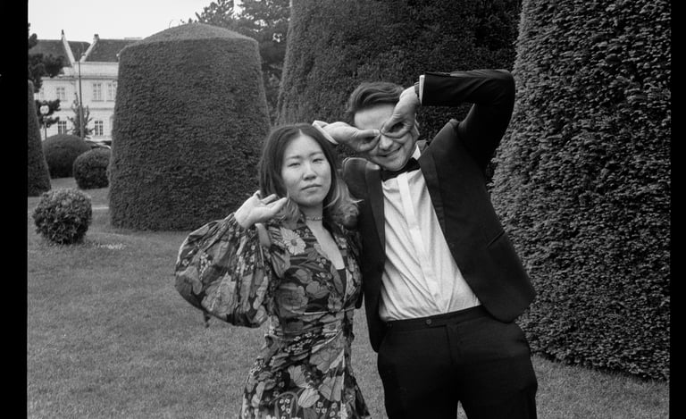 Couple wearing party clothes in a park posing quirky. B&W film photo.