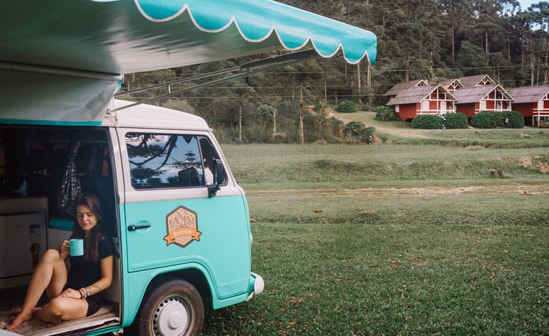 Uma pessoa sentada bebendo café dentro de uma kombi home, estacionada em um jardim.