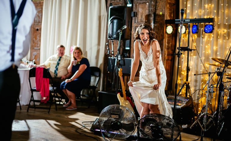 Bride cooling off with fans at Battersea Arts Centre, laughing as guests watch the playful wedding moment unfold.