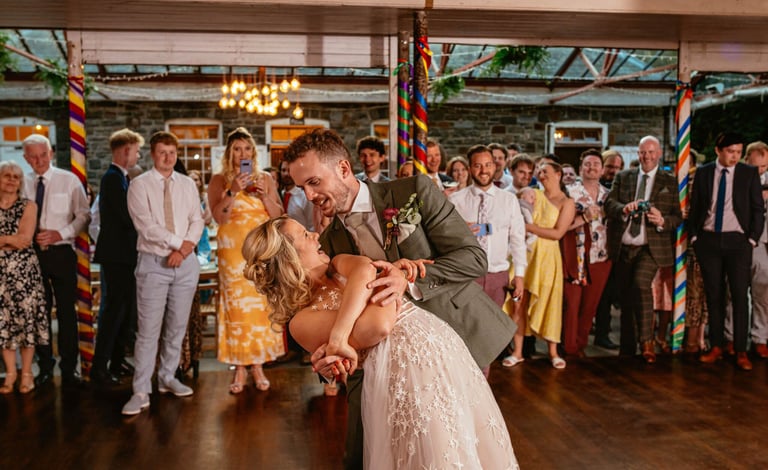 First dance dip at Plas Dinam Country House, the couple beaming as guests cheer them on in the vibrant reception hall.