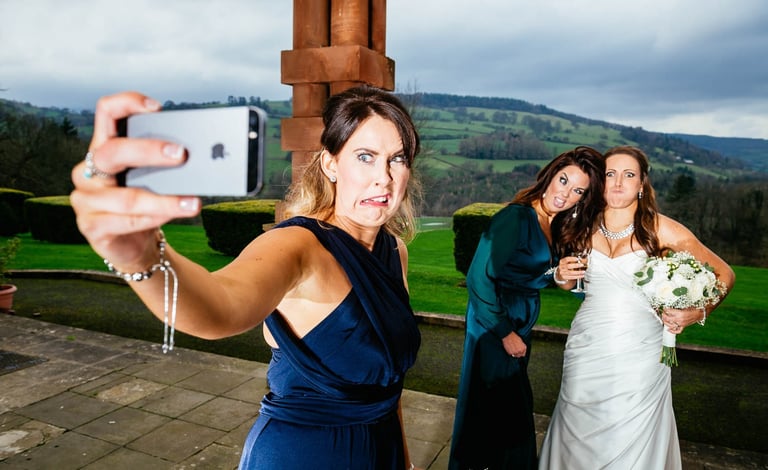 Bridesmaid taking funny selfie with bride and guest at South Wales wedding, captured candidly by photographer Owen Mathias