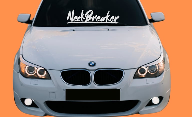 White BMW sedan with NeckBreaker windshield decal and halo headlights on an orange background.