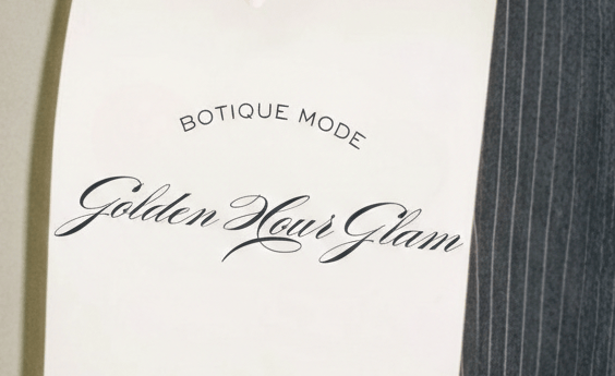 Mano sosteniendo una invitación Golden Hour Glam de Botique Mode sobre un pantalón de raya.