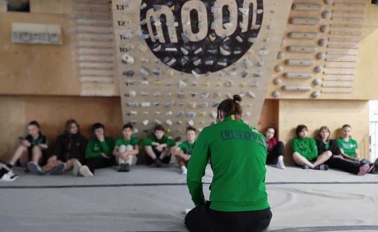 a man in a green jacket sitting in a front of a climbing wall