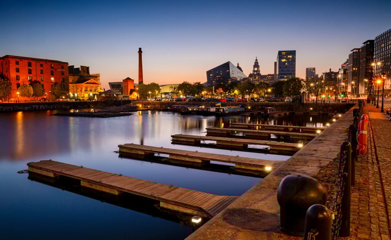 Liverpool's Royal Albert Dock at sunset with empty wooden piers and city skyline lights.
