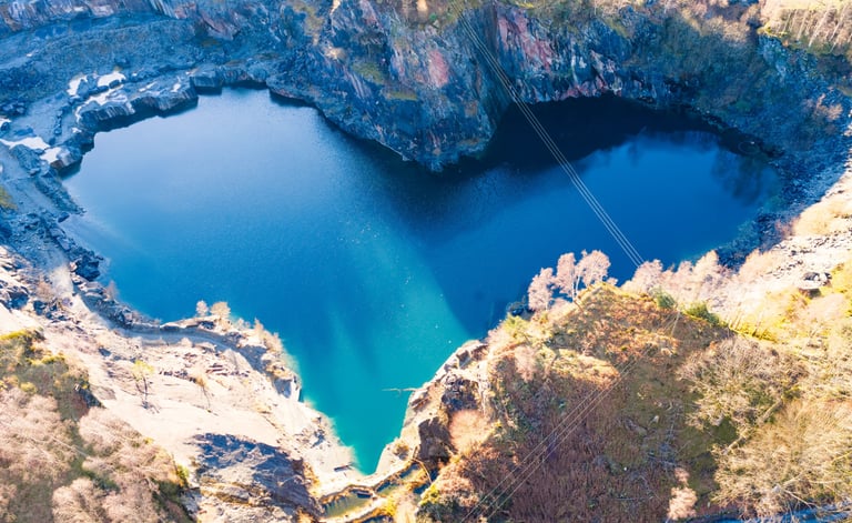 Aerial view of a heart-shaped blue lake surrounded by rocky quarry cliffs 