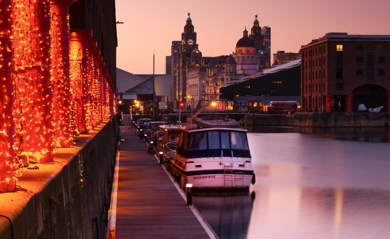 Royal Albert Dock Liverpool at sunset with festive lights, boats, and the Liver Building skyline.