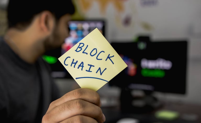 A man facing away from the camera holding up and post it note that says, "Blockchain".