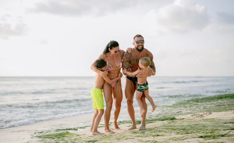 Family sharing a warm embrace on the shoreline rocks during a family photo session at Dreamland Beach Bali.