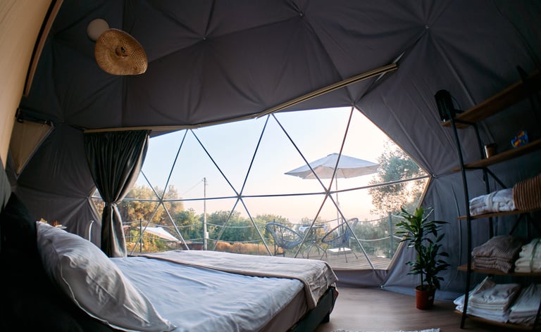 Innenraum der Glamping-Kuppel mit Bett und Panoramablick aufs Meer
