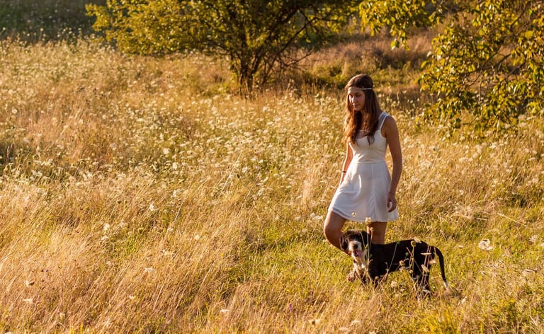 Young girl walking through a field of long grass with a dog