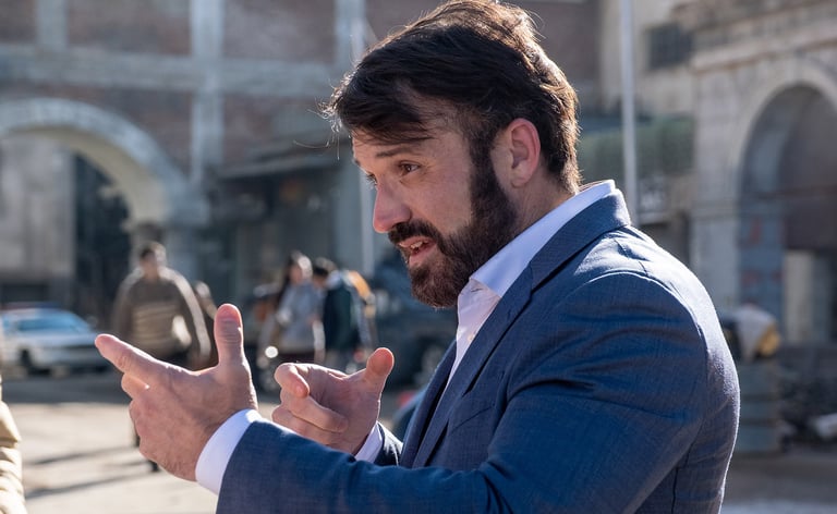 Photo of the side profile of an actor (in a suit) explaining to someone outside the image left side