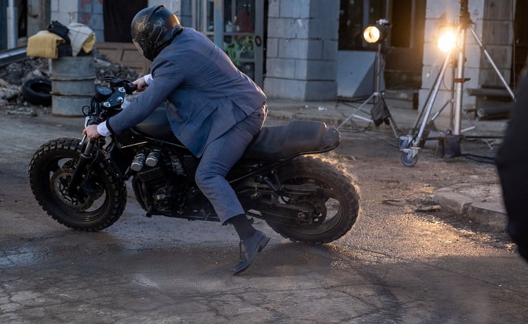 Stuntman on motorbike doing a wheel slide set off in front of main camera moving off left of image 