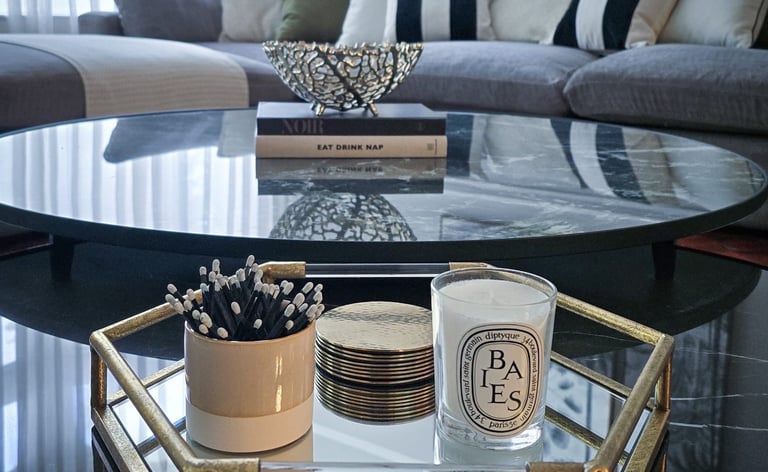 elegant, mirrored, circular coffee table with a tray, books and candles, set against a sofa backdrop