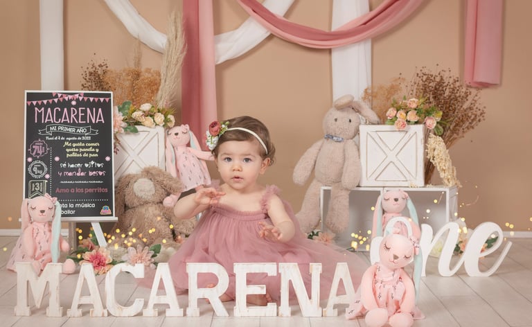 a baby girl in a pink dress sitting on a wooden floor