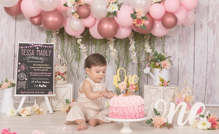 a baby girl in a pink dress and a pink cake