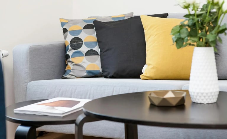 Modern grey sofa styled with yellow, black, and geometric pattern throw pillows near a coffee table.