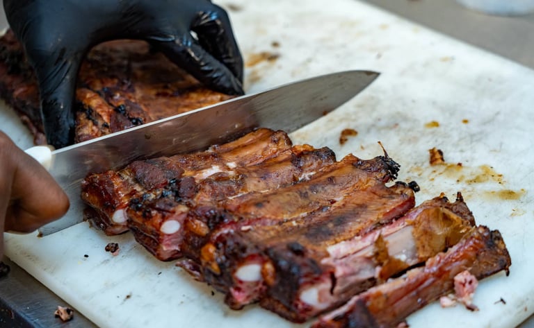 Chef in black gloves slicing smoked BBQ pork ribs on a white cutting board.