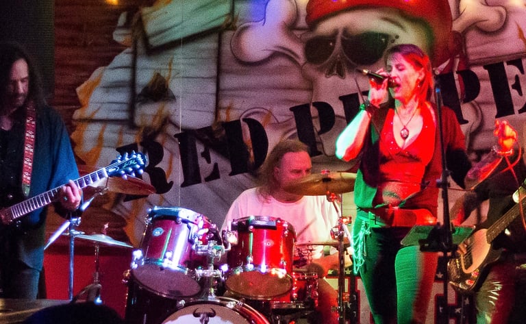 Live rock band performing on stage with female vocalist, guitarist, and drummer at Red Pepper venue.