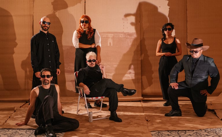 A diverse musical band wearing sunglasses posing against a cardboard backdrop with dramatic shadows.
