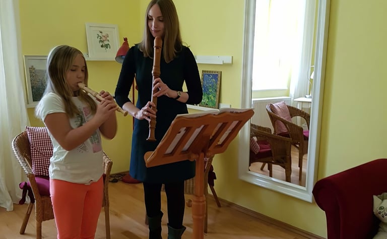 Junges Mädchen spielt auf einer Blockflöte, während die Musiklehrerin auf die Grifftechnik achtet