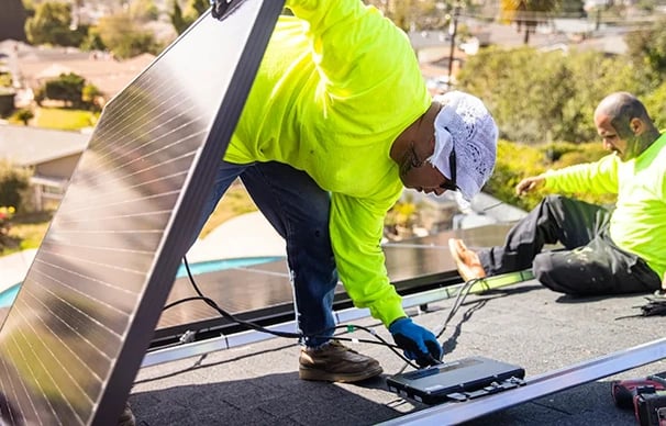 Professional technicians in safety gear installing solar panels on a residential rooftop.