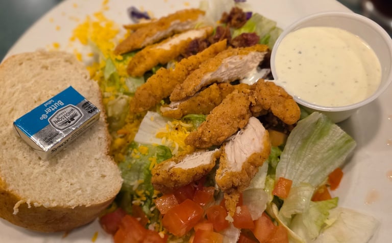 salad with friend chicken on top with ramekin of ranch and bread