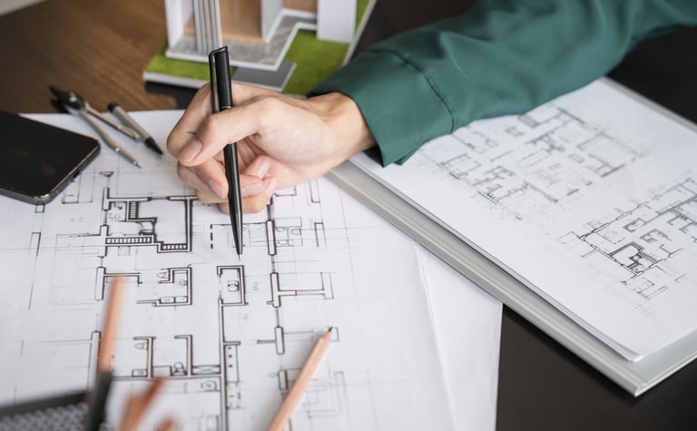 Architect sketching on a detailed house floor plan blueprint with a pen at a wooden desk.