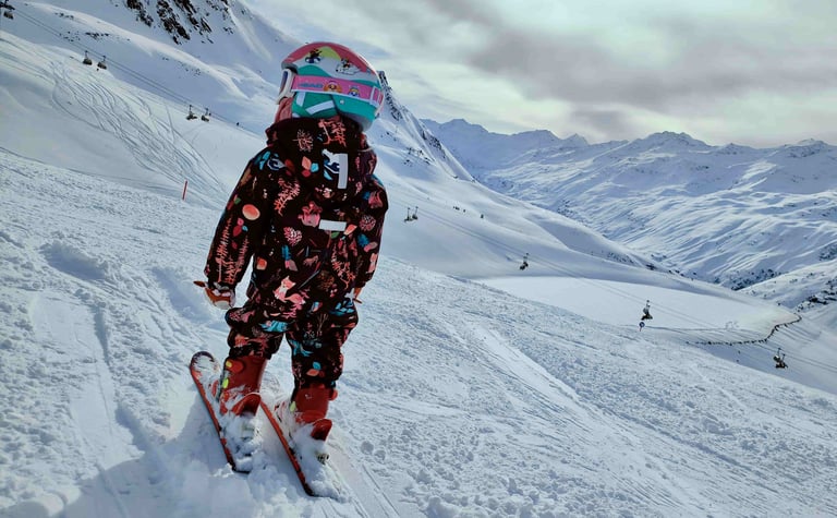 a baby in a snowsuit is standing on a snowy hill