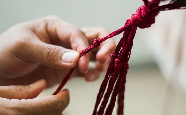 Manos atando un nudo con cordón de algodón rojo para un proyecto artesanal tradicional hecho a mano.