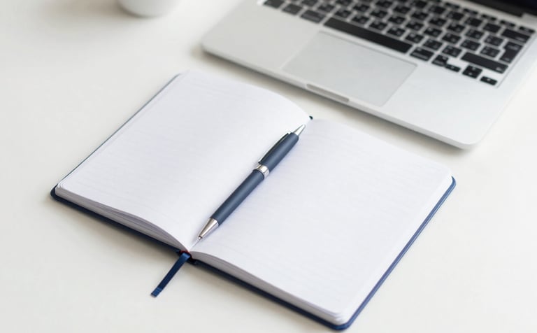 A professional and clean top-down view of an organized desk with a notebook, a pen, and a laptop. The lighting is soft and natural. The color palette features whites and soft blues (#A0C2D9), reflecting a clear and concise work environment.