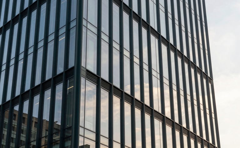 A professional architectural shot of a sleek glass office tower in a metropolitan area. The facade reflects a mist white sky. The structure uses dark charcoal green steel beams for a modern, industrial-minimalist look. Shot at sunset to emphasize transparency.