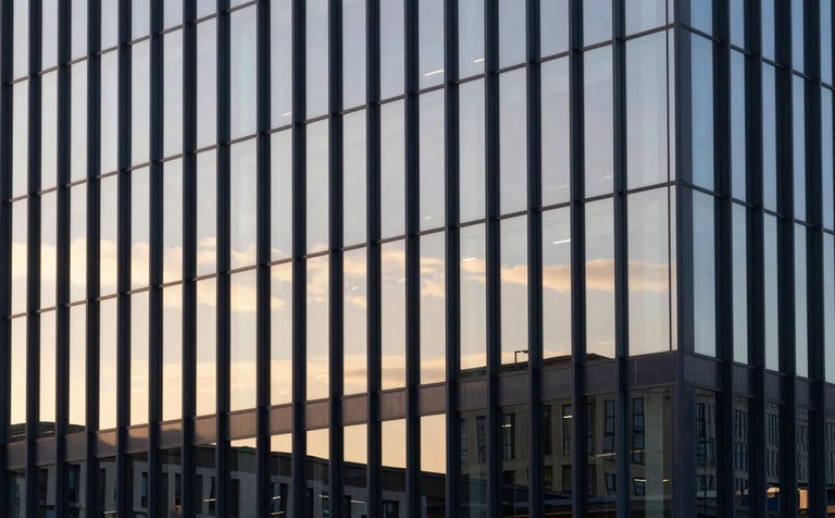 A high-end, minimalist architectural shot of a modern glass office building reflecting a soft gold sunset. The composition is clean and geometric, conveying stability and corporate scale, with dark navy blue shadows in the structural lines.