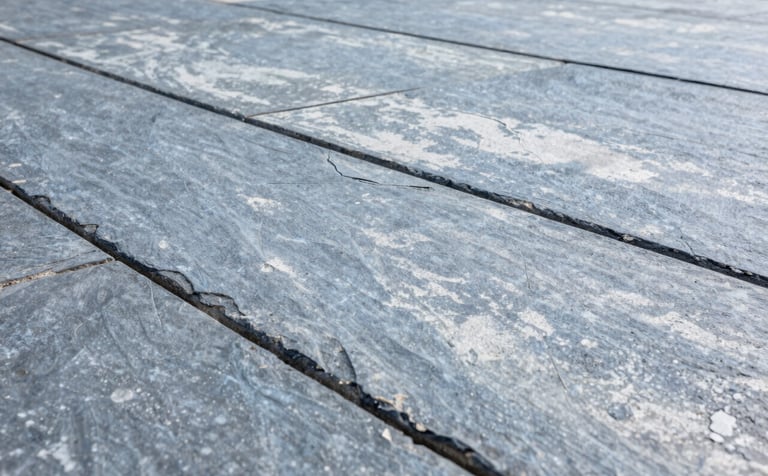 A close-up photograph of a precision-stamped concrete patio with a slate texture. The concrete has a clean, Steel Blue Grey and Soft Cloud White finish. The composition is sharp, showing the intricate grout lines and texture under bright, natural daylight, reflecting robust reliability.