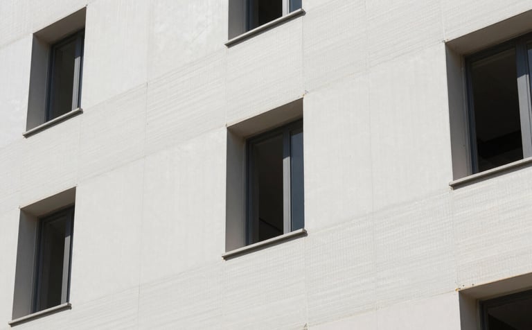A close-up photograph of a clean, modern building facade in Southern Europe being renovated with white high-density EPS insulation panels. Professional construction site, bright daylight, showcasing a sophisticated and efficient installation process with a focus on precision and responsibility.