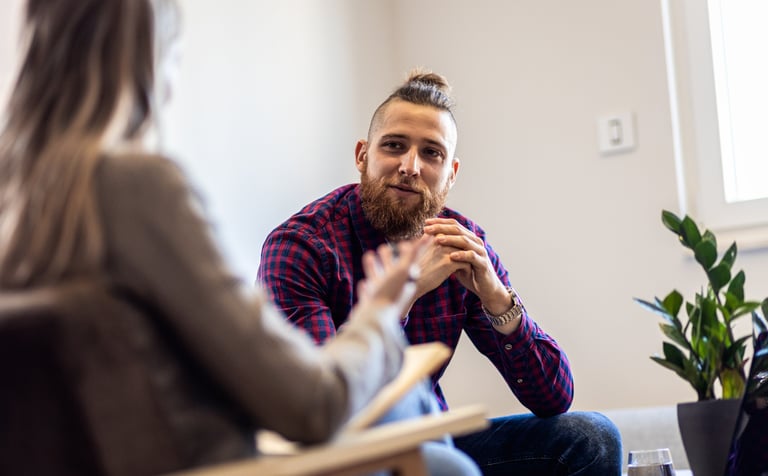 A young man with a beard facing a women in a therapy session