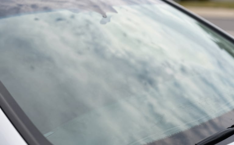 A detailed close-up of a flawless, newly repaired windshield reflecting a bright North American sky and soft off-white clouds. The image emphasizes clarity, safety, and perfection. The composition is clean and minimalist, showing the high-quality finish of the glass.