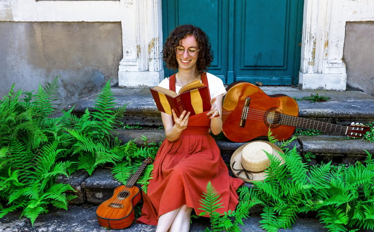 musicienne en train de lire un livre/a woman in a red dress reading on stairs with guitar beside her