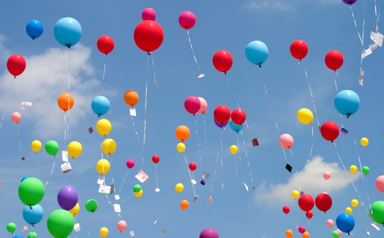 Ballons multicolores s’envolant dans le ciel, porteurs de messages d’amour et d’adieu.