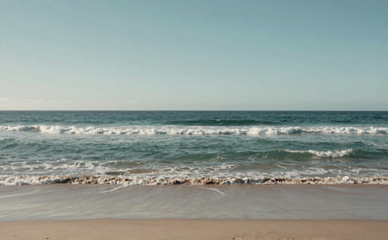 A wide, peaceful landscape of an Australian coastline with gentle waves and soft sand under a clear, pale sky. The composition is grounded and sophisticated, using muted teal and grey-green tones to evoke confidence.