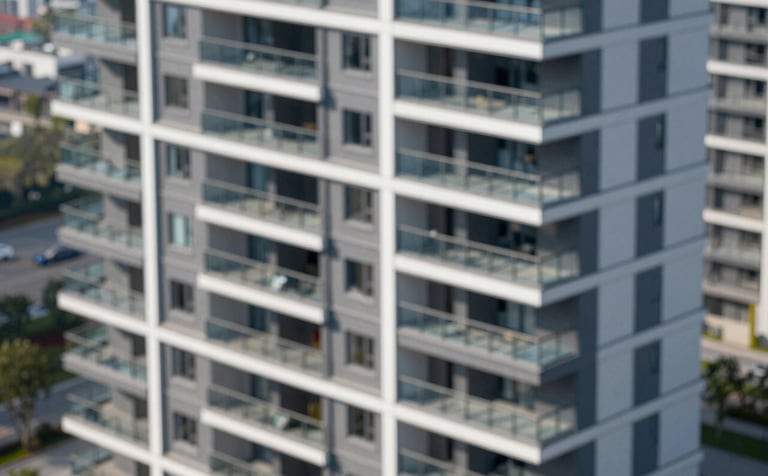 A high-angle architectural shot of a modern, clean apartment complex with sharp lines and glass balconies. The lighting is crisp daylight. Tones of #4C6A7F and #1A2C3D are reflected in the windows and shadows, conveying a sense of organized property management.