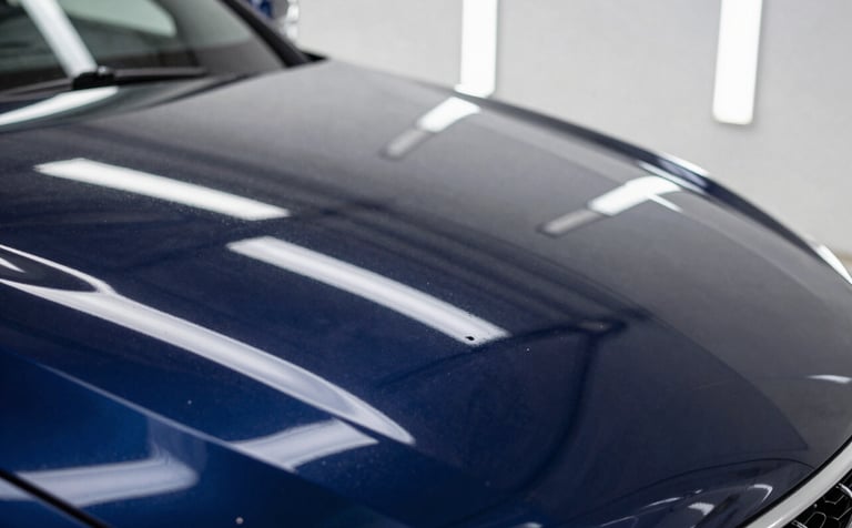 Macro photography of a deep navy blue car hood in a North American studio. The paint reflects a perfect, mirror-like image of the overhead lights after a professional ceramic coating. The gloss is deep and liquid-like, showcasing ultimate precision.