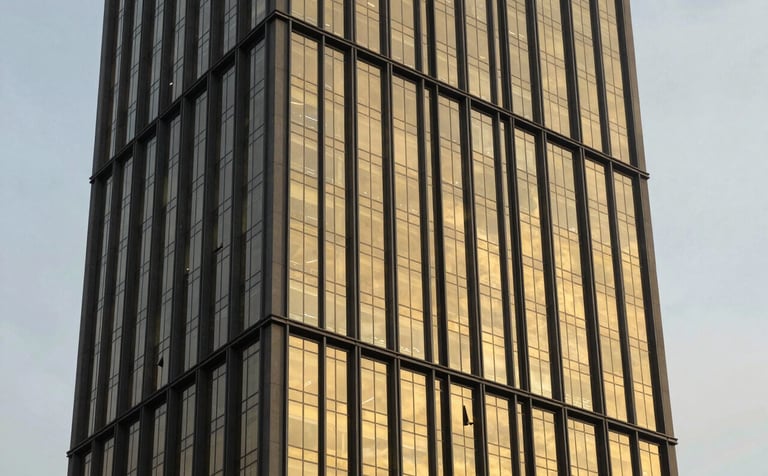 A sharp architectural photograph of a contemporary commercial skyscraper in Abuja. The building features dark charcoal metal frames and gold reflective glass catching the setting sun.