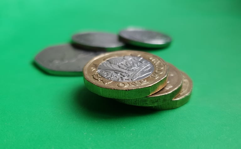 A close-up shot of British one pound coins stacked on a bright green surface.
