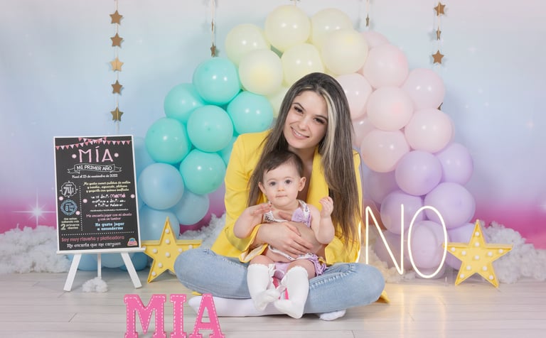 a woman holding a baby in front of a rainbow colored backdrop