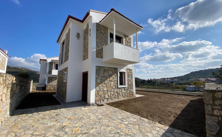 Modern white and stone-clad two-story villa with a balcony under a bright blue sky.
