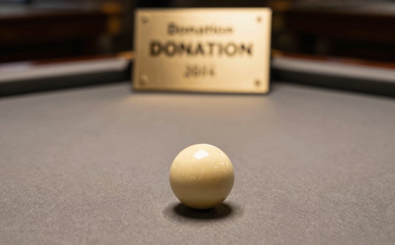 A sophisticated close-up of a pool table with a donation plaque visible in the blurred background. The lighting is warm and soft, emphasizing the professional felt texture and muted gold billiard accessories.