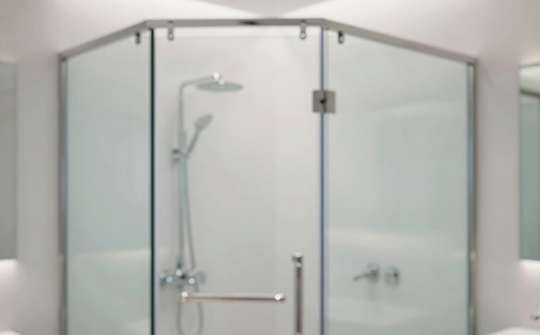 A close-up of a high-end minimalist bathroom featuring a frameless tempered glass shower enclosure. The scene is bright and clean, with soft lighting reflecting off the polished glass and silver fixtures. Incorporates brand colors #F7F9FB and #BCC9D4 for a sophisticated, modern feel.