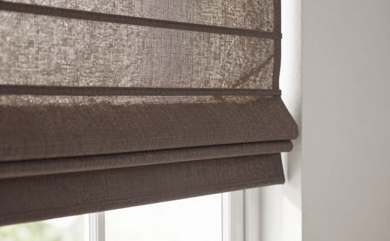 Close-up photography of custom Roman shades in a muted brown fabric, installed in a bright North American breakfast nook. The lighting is crisp and natural, showcasing the precise fit and clean lines of the blinds against a soft white wall.