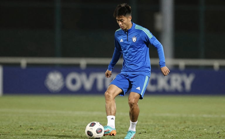 Action shot of a young player in #8FAABF blue training gear, focusing on the ball during an evening practice session under stadium lights. Professional, high-performance aesthetic.